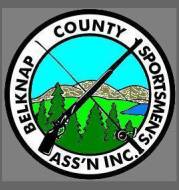 Circular logo for Belknap County Sportsmen's Association featuring a rifle, fishing rod, trees, hills, and a small body of water.